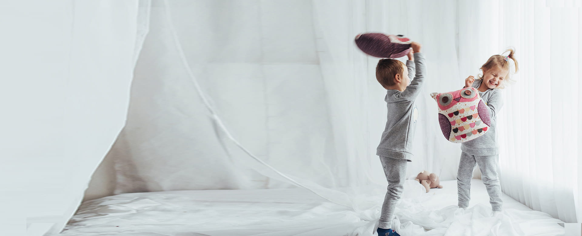 Twee kinderen hebben pret met een kussengevecht bij hen thuis: de verzekering Ongevallen Privéleven dekt hen bij een ongeval.
