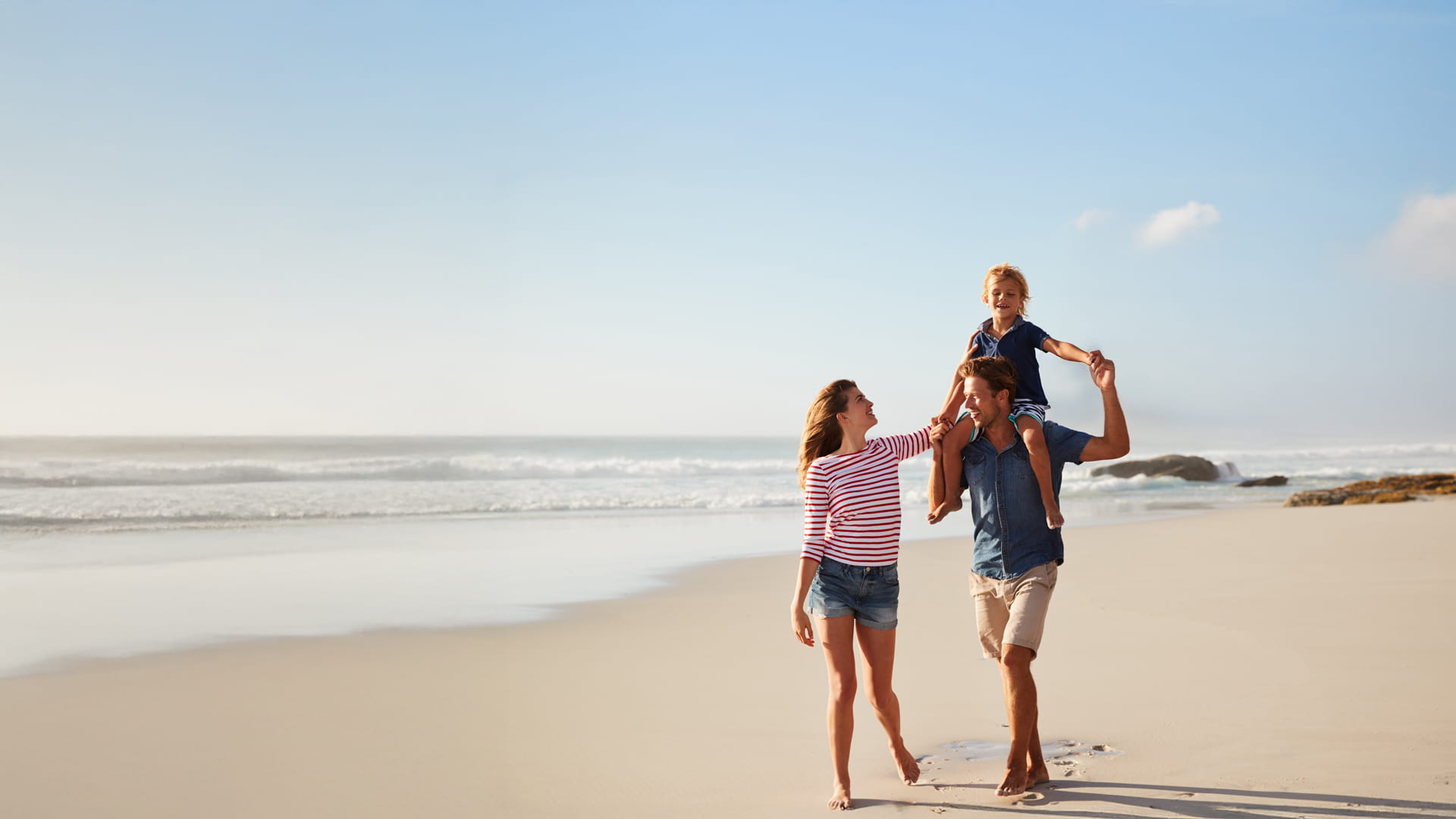 Ouders en hun kind genieten volop van een strandwandeling dankzij de AXA Reisverzekering.