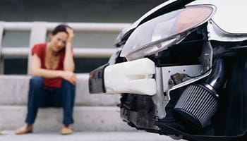 Vrouw zittend naast haar beschadigde auto na een ongeluk.