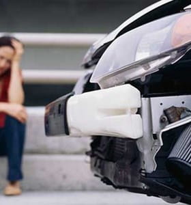 Vrouw zittend naast haar beschadigde auto na een ongeluk.