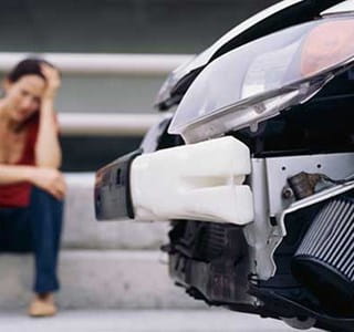 Femme assise à côté de sa voiture endommagée à la suite d’un accident.