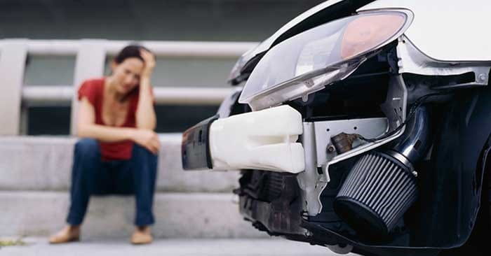 Femme assise à côté de sa voiture endommagée à la suite d’un accident.