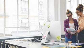 Deux femmes dans un espace de coworking qui examinent les formules d'épargne pour une pension complémentaire destinées aux indépendants débutants.