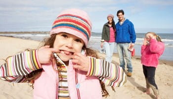 Een gezin met twee kinderen geniet van een zorgeloze strandwandeling dankzij de bescherming van hun familiale en ongevallenverzekering.