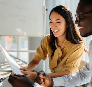 Deux collègues consultant ensemble un document devant un ordinateur portable, illustrant une situation professionnelle liée à la continuité d’activité d’un dirigeant ou indépendant immobilisé temporairement.