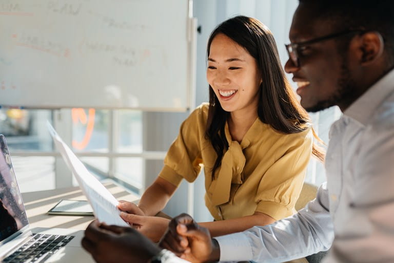 Deux collègues consultant ensemble un document devant un ordinateur portable, illustrant une situation professionnelle liée à la continuité d’activité d’un dirigeant ou indépendant immobilisé temporairement.