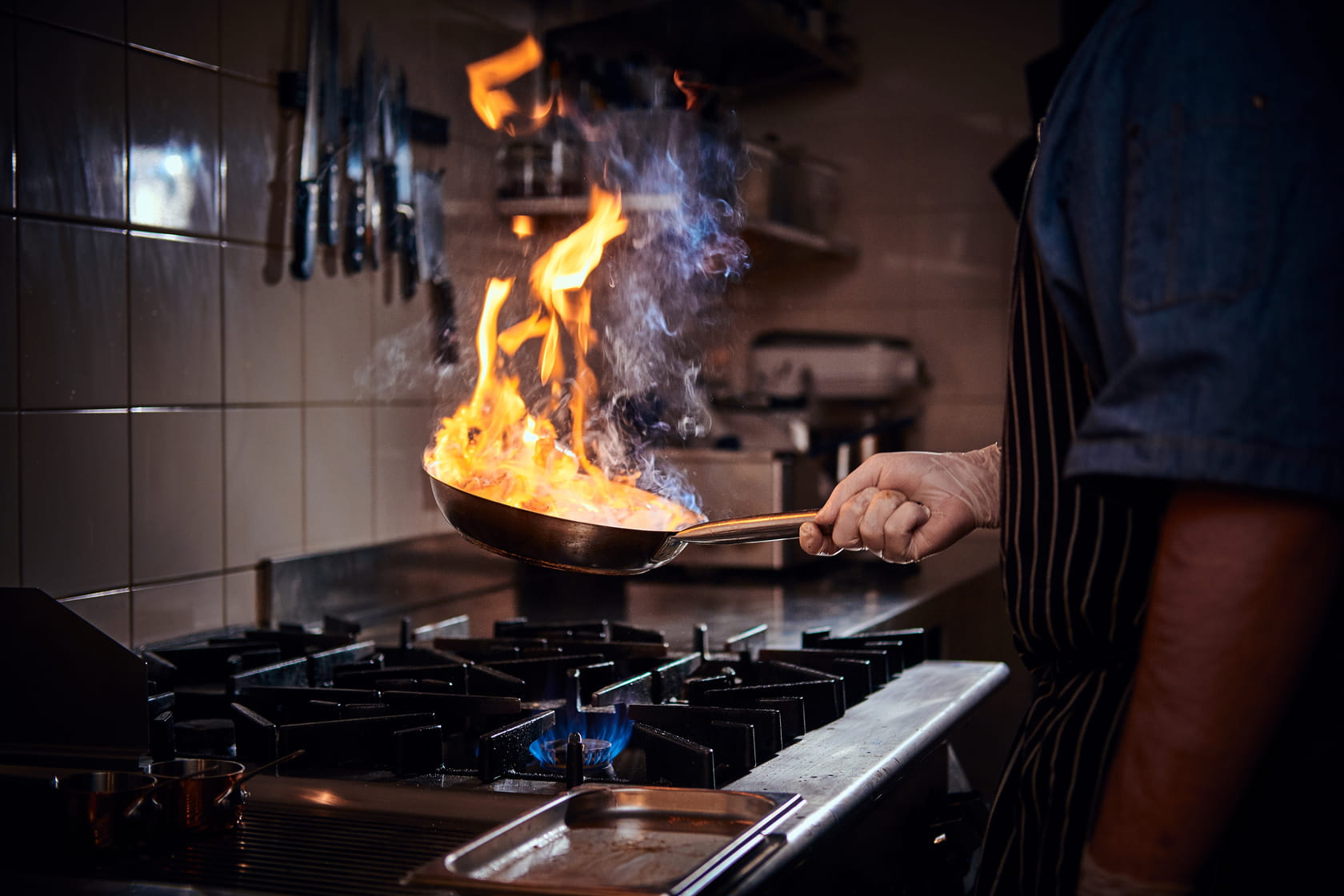 Persoon heeft tijdens het koken een vlam in de pan, wat een belangrijke oorzaak is van woningbranden. 