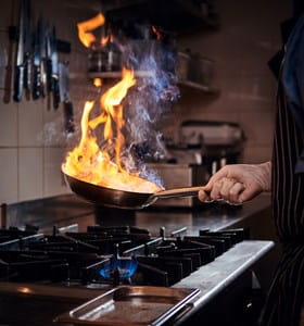 Persoon heeft tijdens het koken een vlam in de pan, wat een belangrijke oorzaak is van woningbranden.