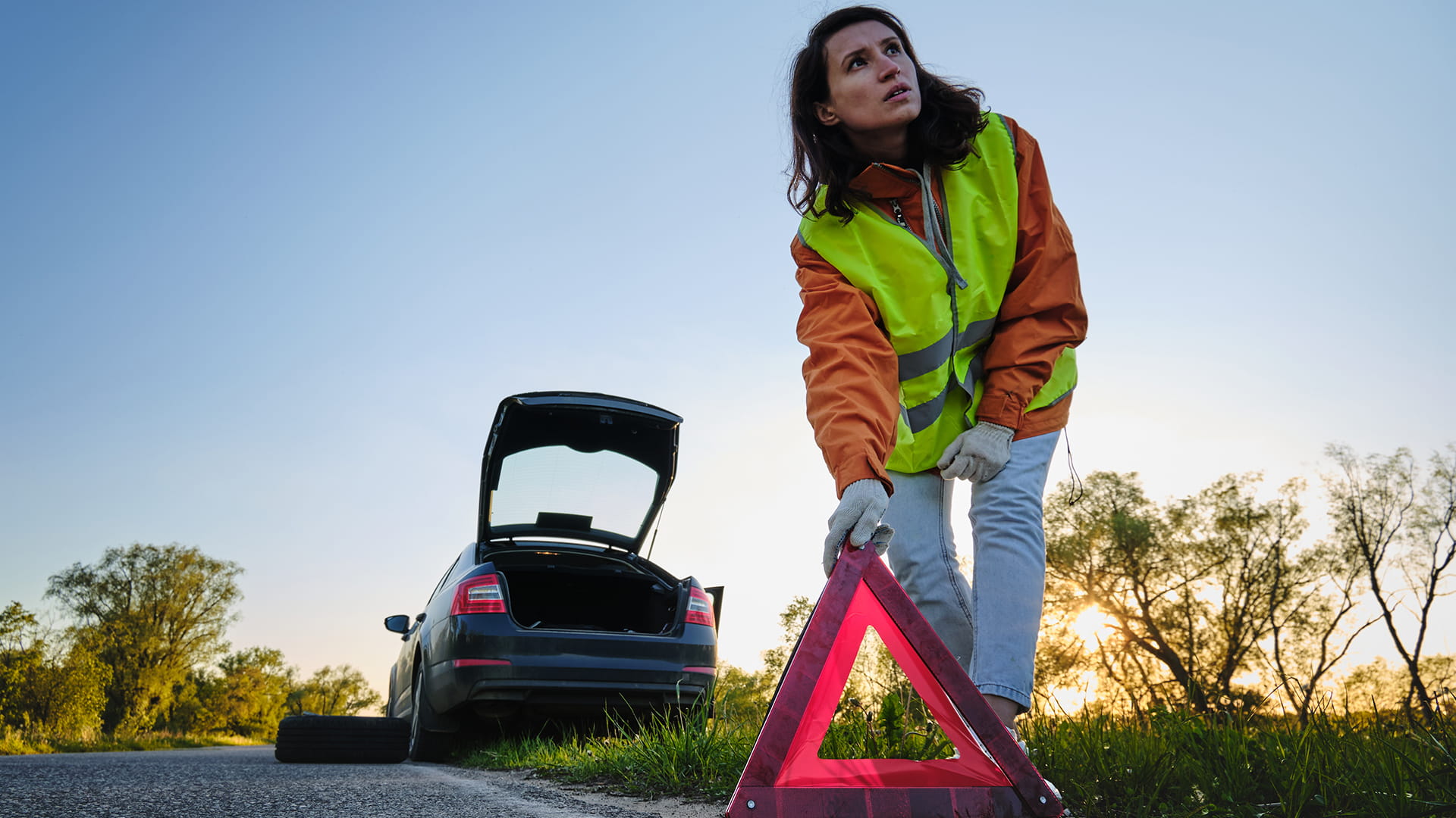 Vrouw vervangt een autowiel na een ongeval en plaatst de gevarendriehoek.