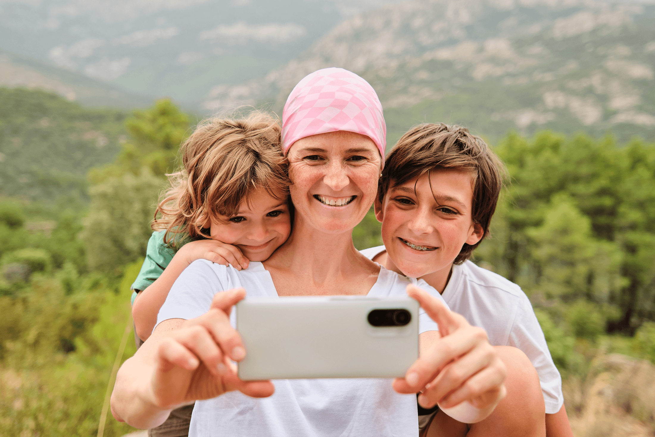 Een vrouw met kanker gebruikt een smartphone om een selfie te nemen met haar zoon en dochter.  