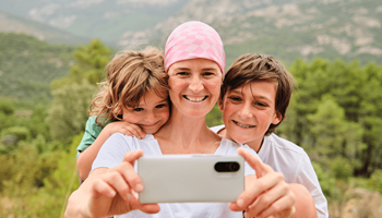 Een vrouw met kanker gebruikt een smartphone om een selfie te nemen met haar zoon en dochter.