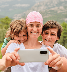 Een vrouw met kanker gebruikt een smartphone om een selfie te nemen met haar zoon en dochter.