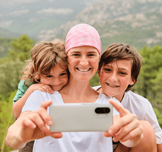 Een vrouw met kanker gebruikt een smartphone om een selfie te nemen met haar zoon en dochter.