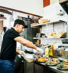 Un membre du personnel de l'horeca prépare et sert des plats selon les directives d'AFSCA et HACCP.