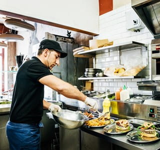 Een horecapersoneelslid bereidt en serveert gerechten volgens de FAVV- en HACCP-richtlijnen.