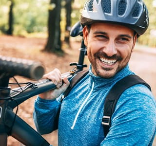 Man met fietshelm lacht omdat hij een autoverzekering per kilometer heeft.