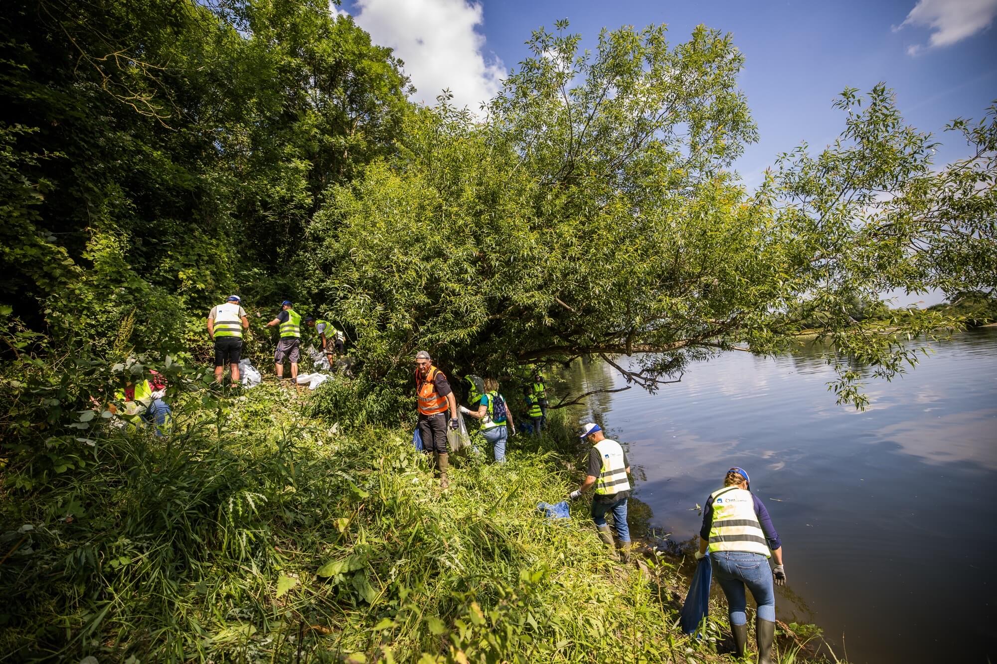 Volontaires équipés nettoyant les berges d’une rivière après une inondation, retirant des déchets dans l’eau et sur les rives en équipe.