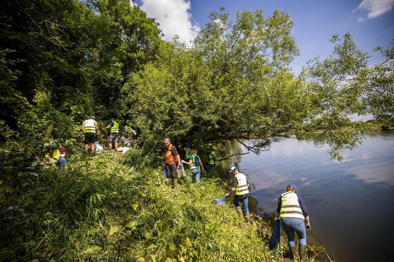 Volontaires équipés nettoyant les berges d’une rivière après une inondation, retirant des déchets dans l’eau et sur les rives en équipe.